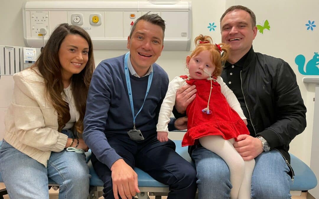 A family sit with a doctor on a hospital bed. The toddler has a tube inserted in one nostril